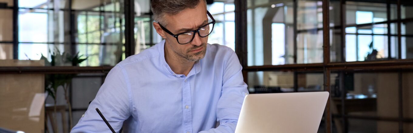 Ondernemer schrijft aan een ondernemingsplan met laptop en notitieboek in een moderne kantooromgeving