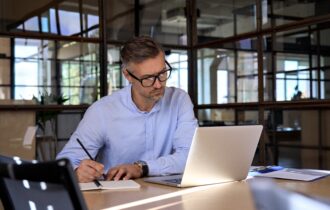 Ondernemer schrijft aan een ondernemingsplan met laptop en notitieboek in een moderne kantooromgeving