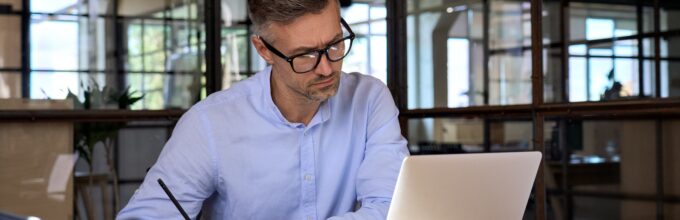 Ondernemer schrijft aan een ondernemingsplan met laptop en notitieboek in een moderne kantooromgeving